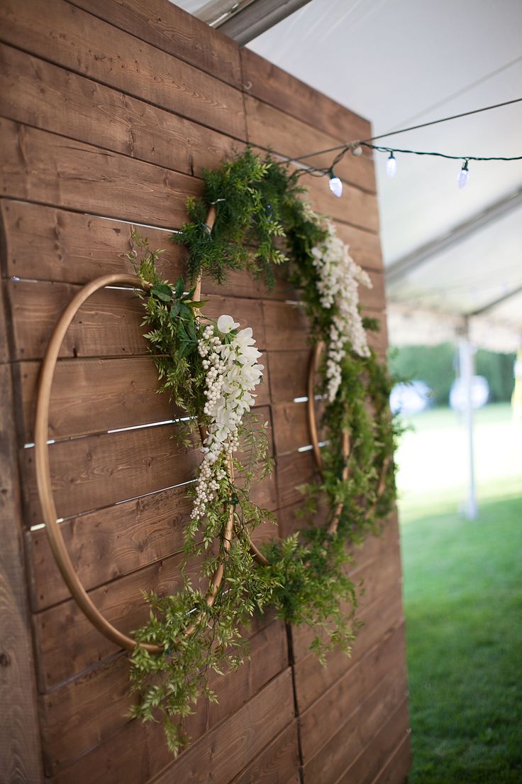 a wooden wall decorated with greenery and white flowers, hanging from it's sides