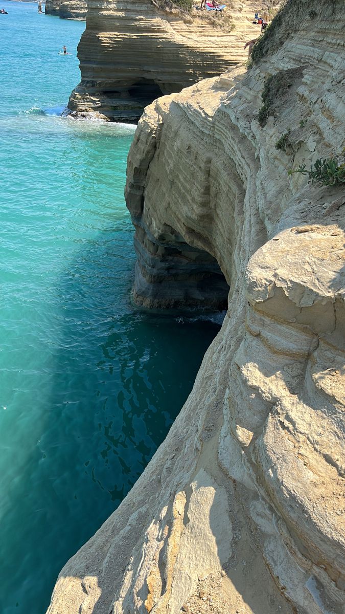 the water is crystal blue and there are two people swimming in the ocean near some cliffs