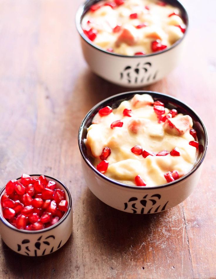 two bowls filled with pudding and pomegranates on top of a wooden table