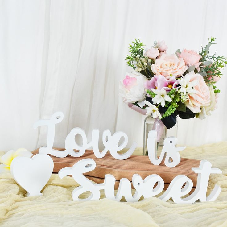 a vase filled with flowers sitting on top of a bed next to a sign that says love is sweet