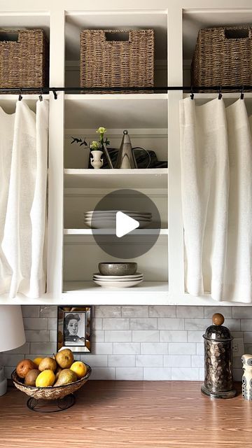 a kitchen with white cabinets and baskets on the counter top, next to a window