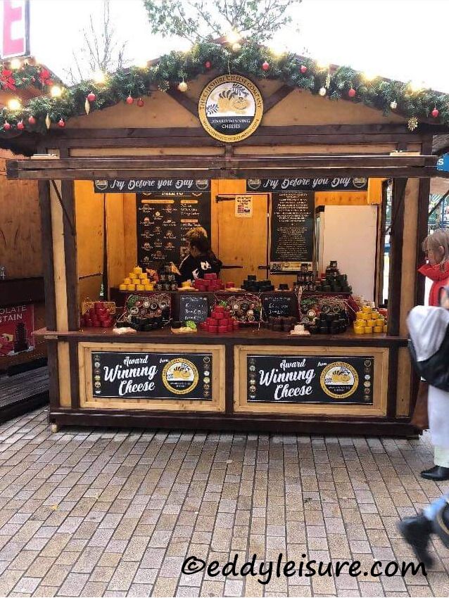 a man walking past a food stand with christmas decorations on the roof and lights above it