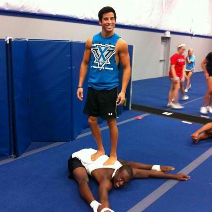 two men standing and laying on the ground in a gym with other people around them