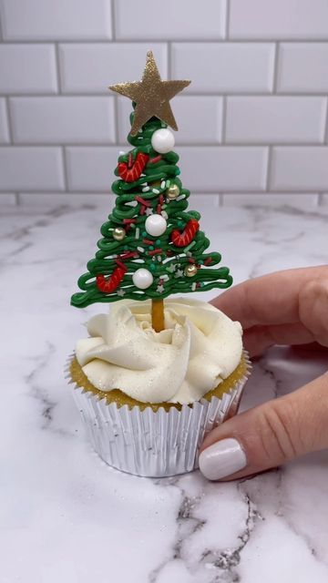 a cupcake with icing and a christmas tree on top is being held by a woman's hand