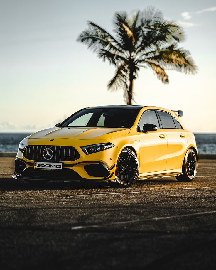 a yellow mercedes benz cla parked in front of a palm tree on the beach