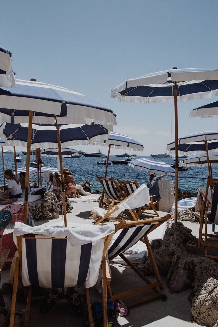 many chairs and umbrellas on the beach with people sitting under them near the water