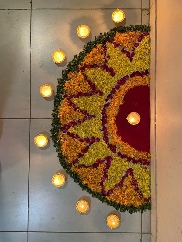 candles are lit on the floor next to a circular arrangement of flowers and leaves that is surrounded by petals