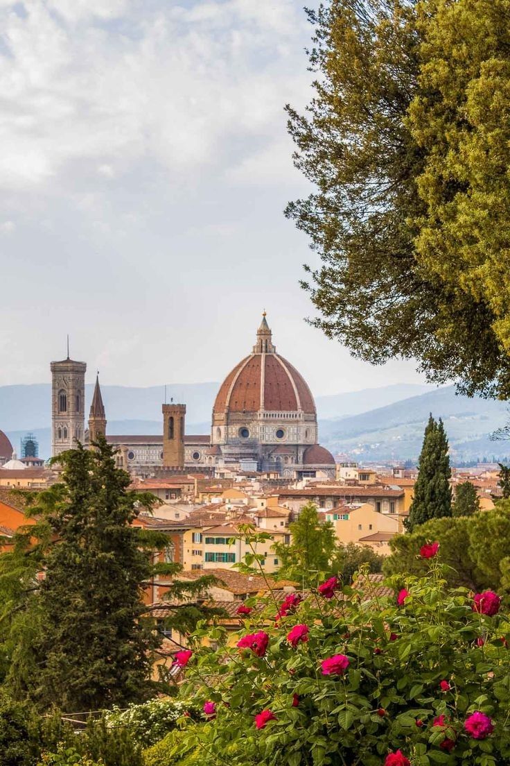 the city is surrounded by trees, flowers and mountains in the distance are some buildings with domes on them