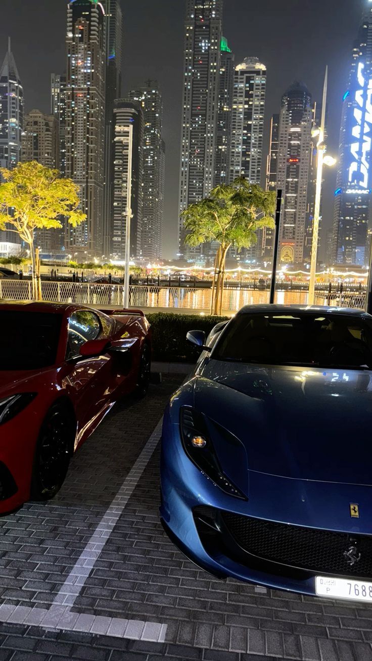 two sports cars parked next to each other in front of a city skyline at night