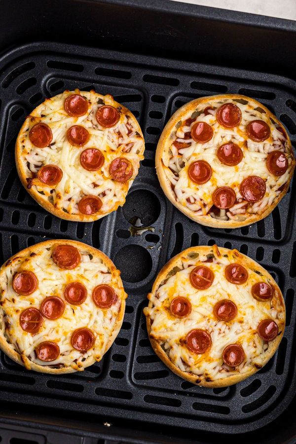 four mini pizzas sitting on top of a black grill grate with cheese and pepperoni