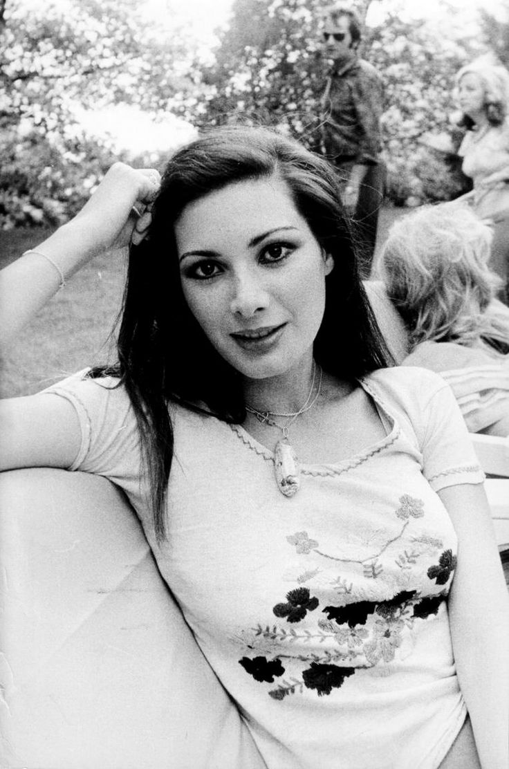 a black and white photo of a woman sitting on a couch in the park with her hands behind her head