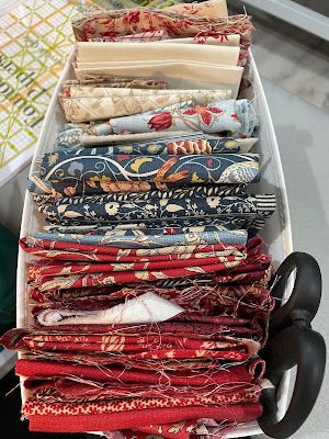 a row boat filled with lots of different fabrics on top of a table next to a sewing machine