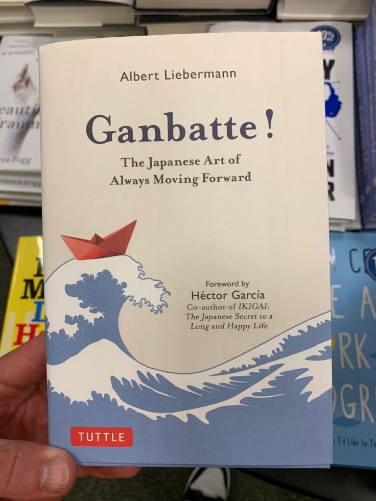 a person holding up a book about gambate in front of bookshelves