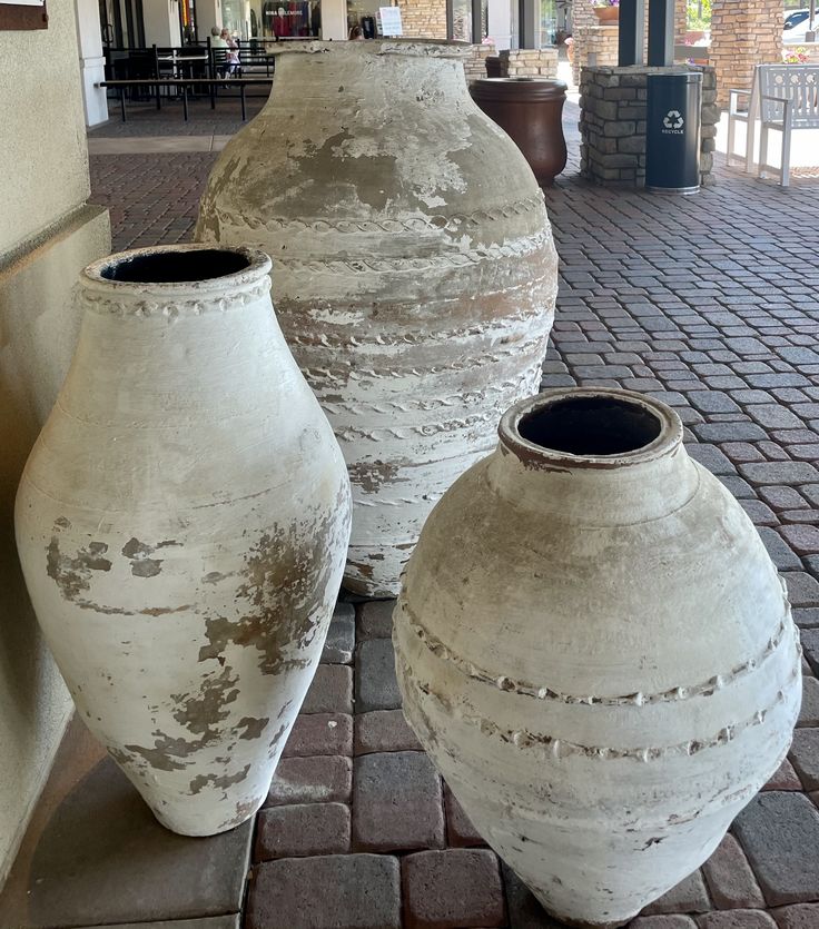 three white vases sitting on the ground in front of a building with brick floors