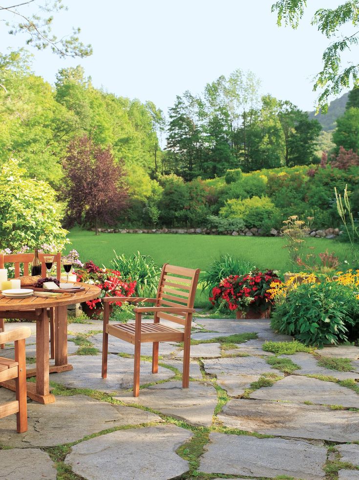 a table and two chairs sitting on top of a stone floor next to a lush green field