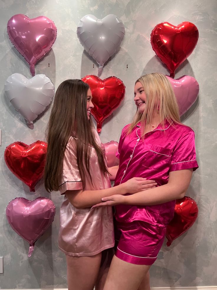 two women in pink pajamas standing next to each other with hearts on the wall behind them