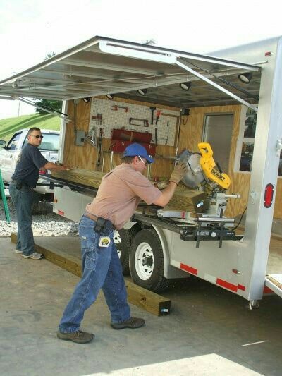 two men are working on the back of a trailer with tools in it and one man is holding a wrench