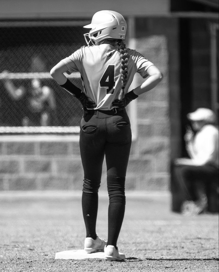 a softball player is standing on the field with her back to the camera and looking down