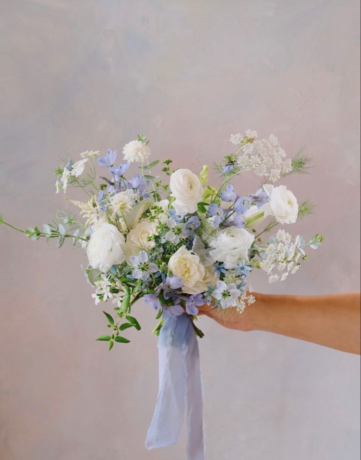 a bouquet of white and blue flowers in someone's hand