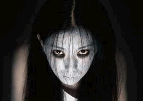 a woman with long black hair and white make - up on her face in the dark