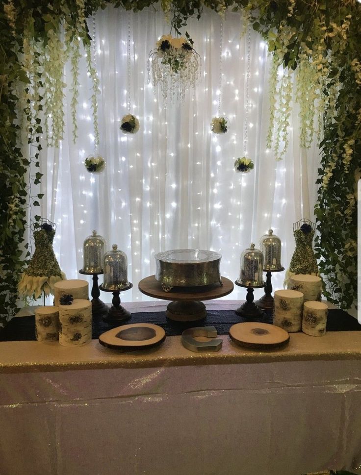 the table is set up with candles and plates on it, surrounded by greenery