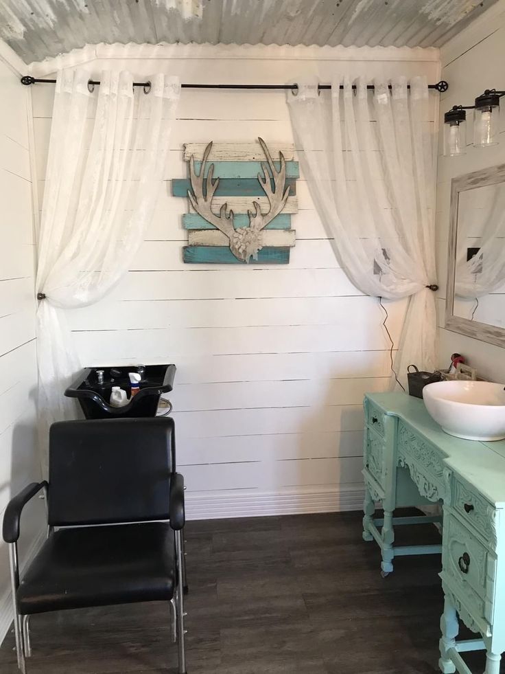 a chair and sink in a room with white walls, wood flooring and curtains