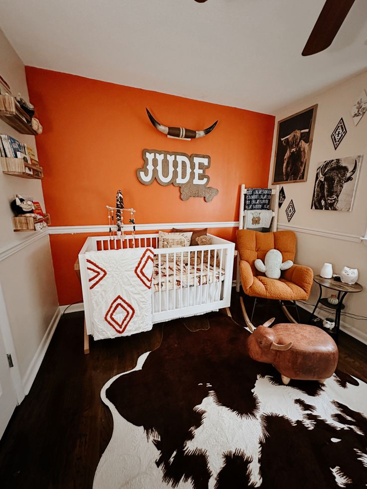 a baby's room with an orange accent wall and cow hide rug on the floor