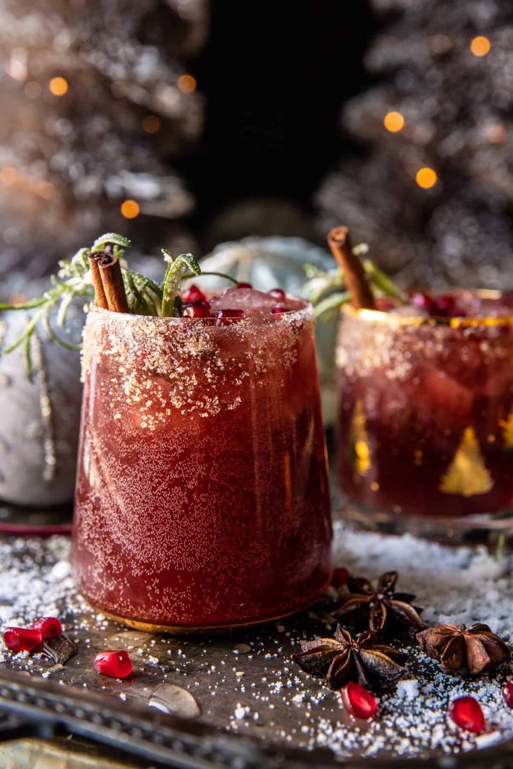 two glasses filled with red drink sitting on top of a metal tray next to a christmas tree