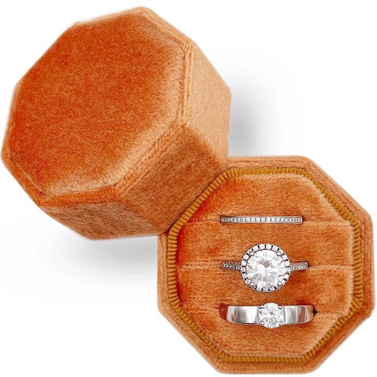 an orange velvet ring box with two rings in it and a diamond on the inside