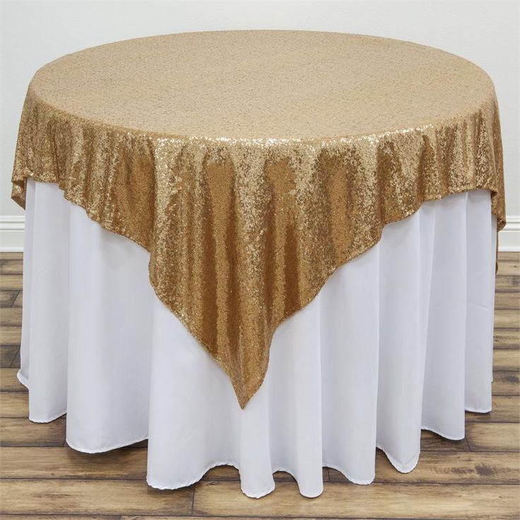 a gold and white table cloth on top of a round table with an overlay