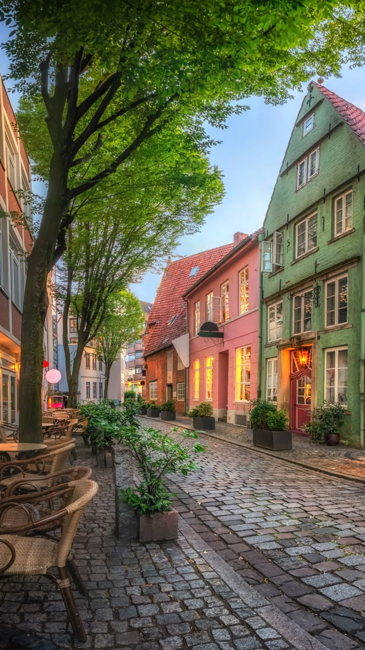 a cobblestone street with benches and tables in the foreground, surrounded by tall buildings