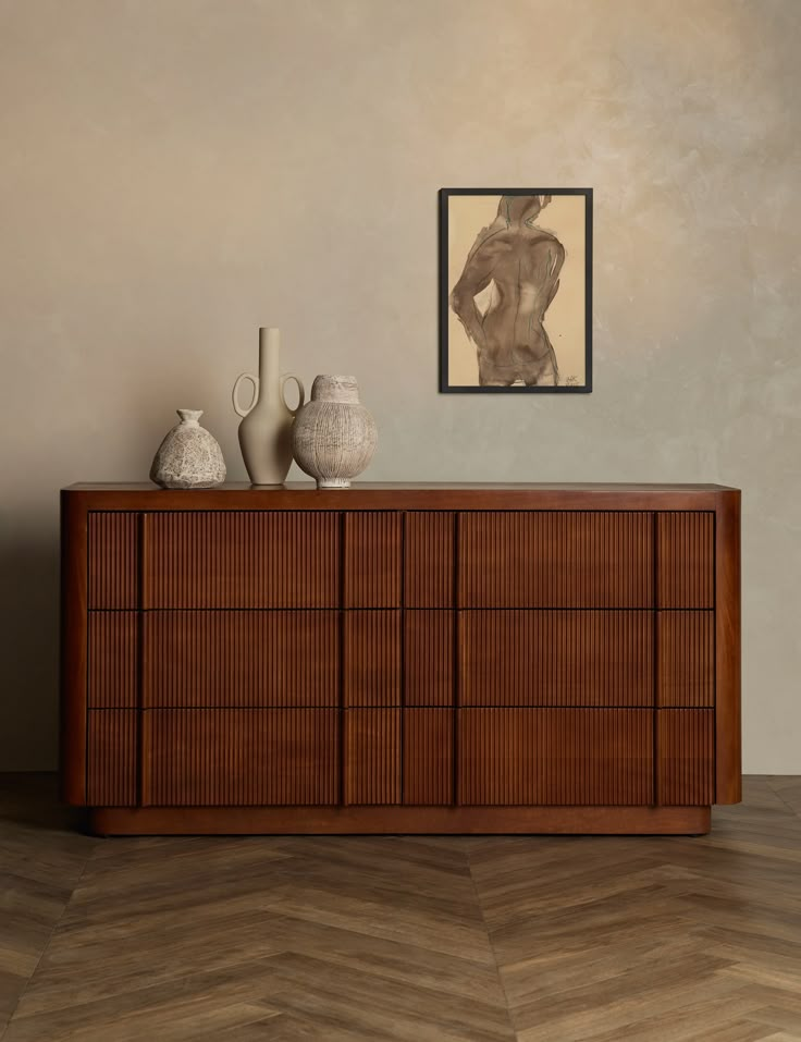 a wooden dresser with vases on it in front of a painting and framed nude figure