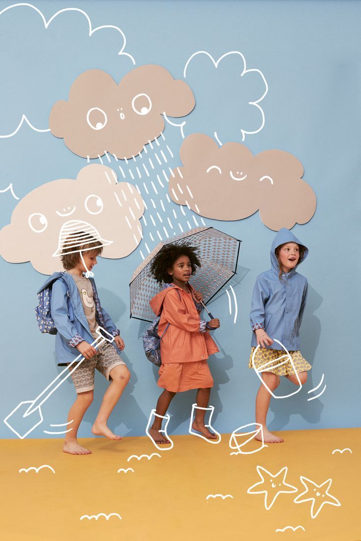 three children standing in front of a wall with clouds and umbrellas