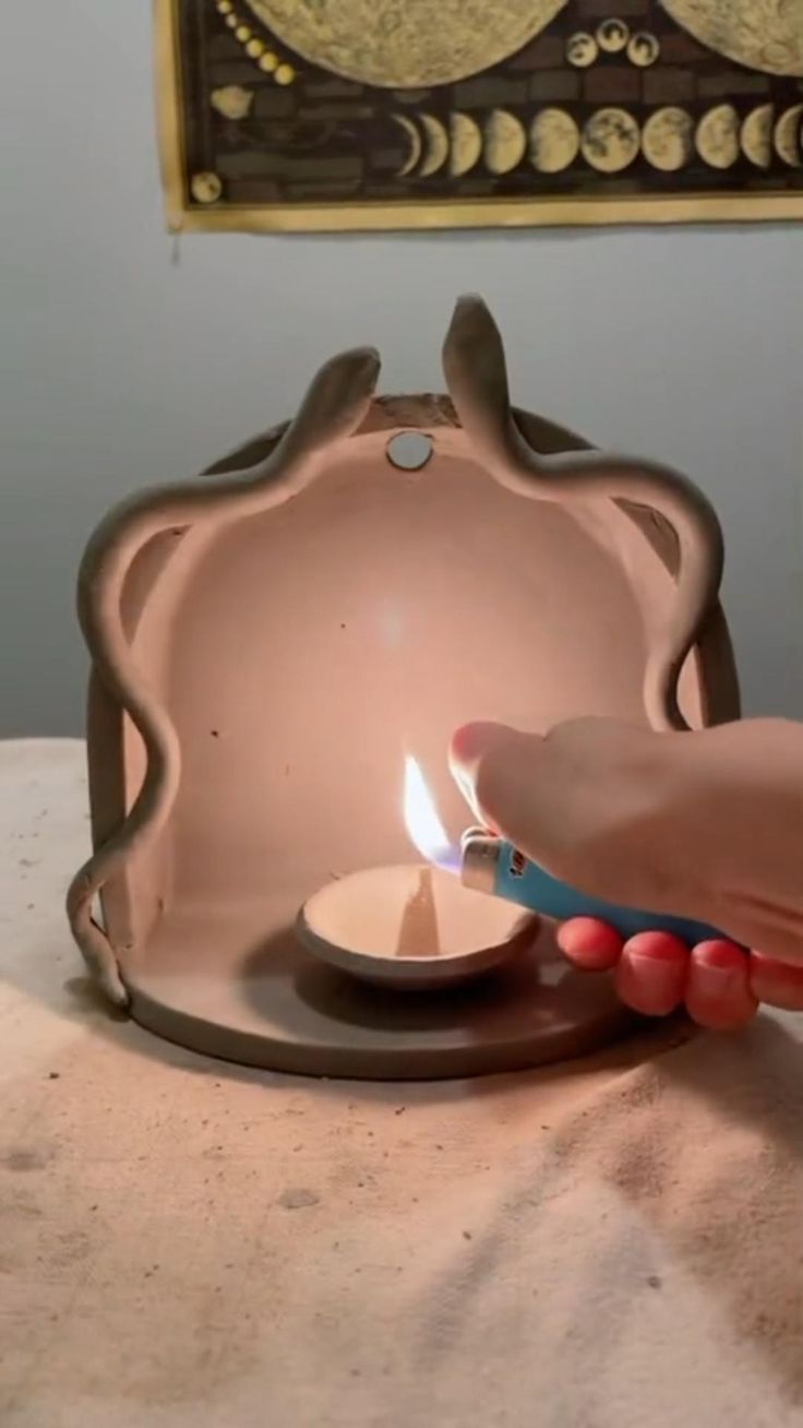 a person lighting a small candle in a pink container on a table with a painting behind it