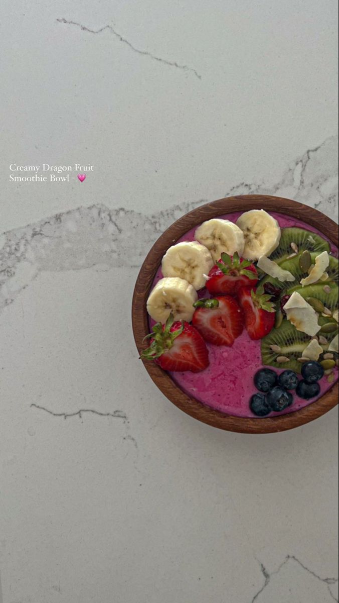 a wooden bowl filled with fruit on top of a white marble countertop next to a pink smoothie