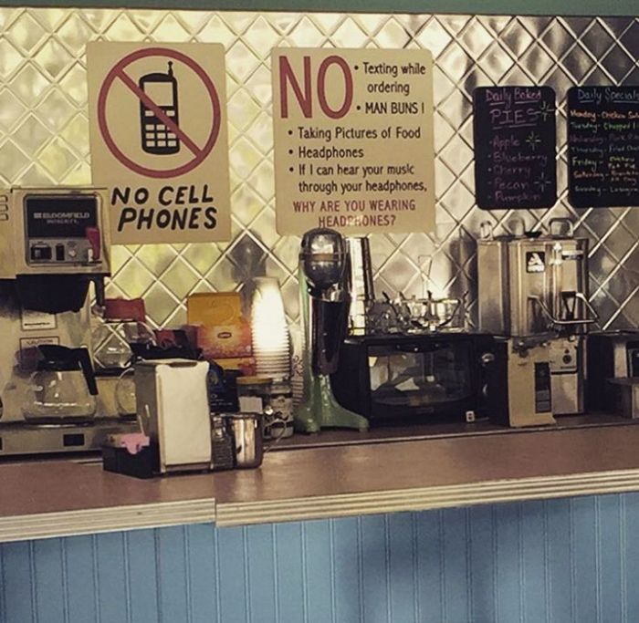 a no cell phone sign on the side of a restaurant counter next to coffee machines