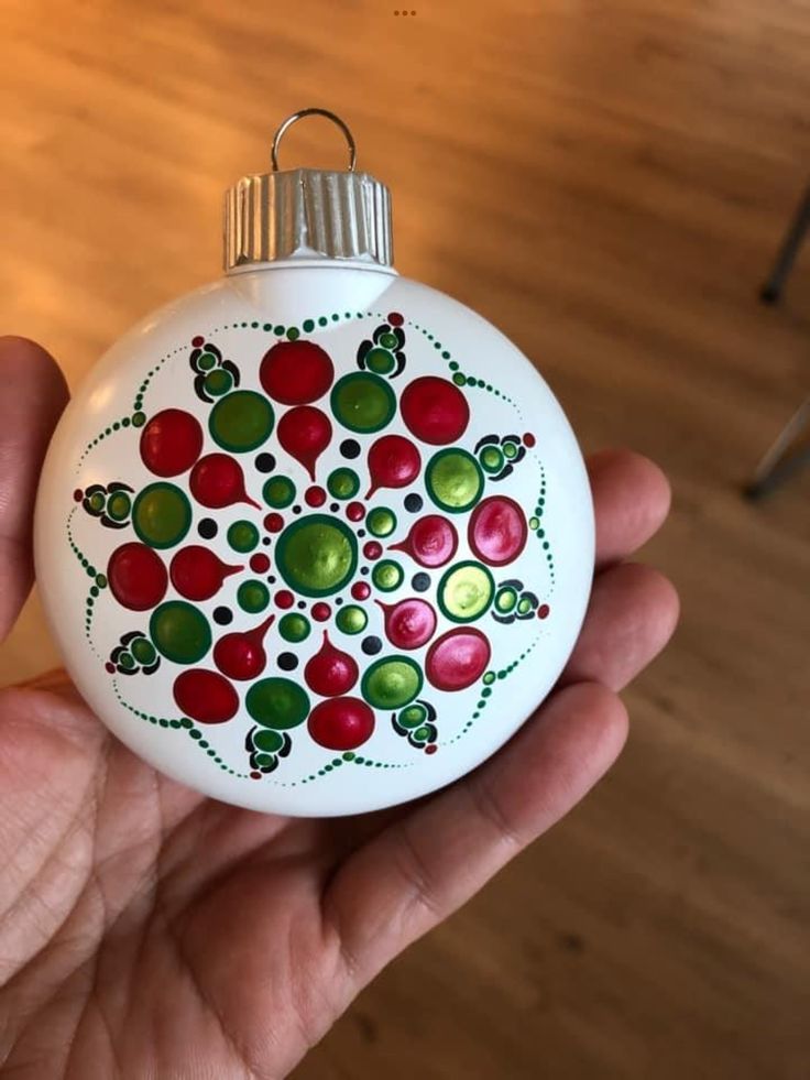 a hand holding a white ornament with red, green and yellow designs on it