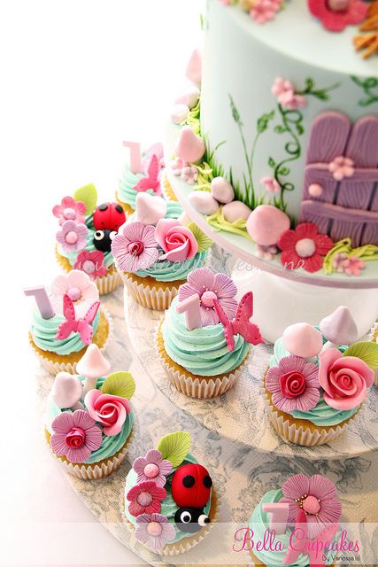 cupcakes decorated with flowers and ladybugs on a cake platter next to a birthday cake