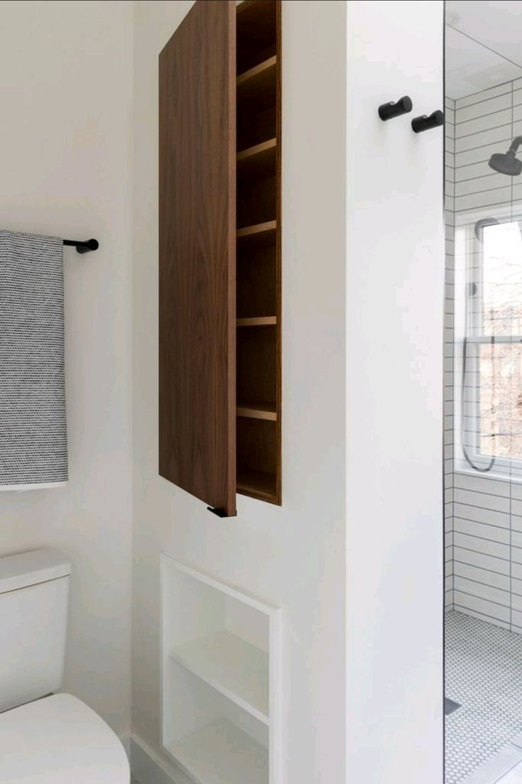 a white toilet sitting next to a wooden cabinet in a bathroom near a shower stall