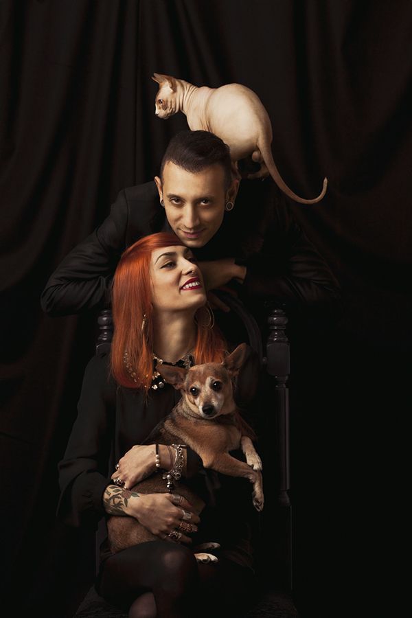 a man and woman sitting in a chair with a cat on their shoulders, both holding a dog