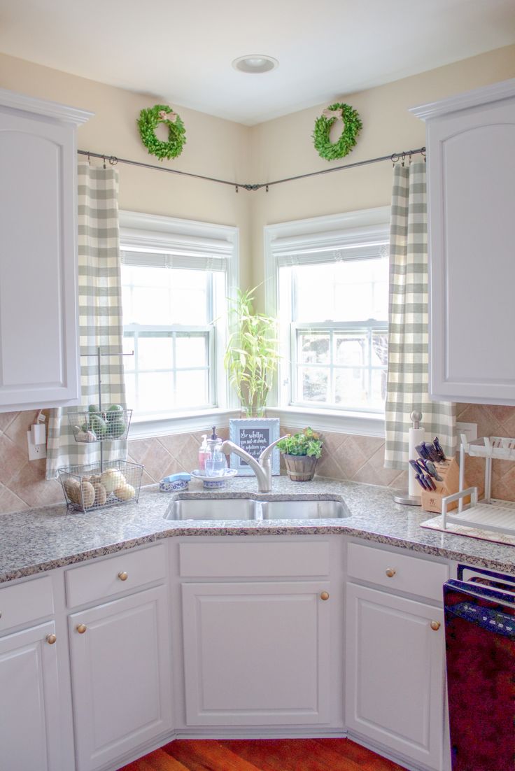 a kitchen with white cabinets and counter tops in front of two windows that have green wreaths on them