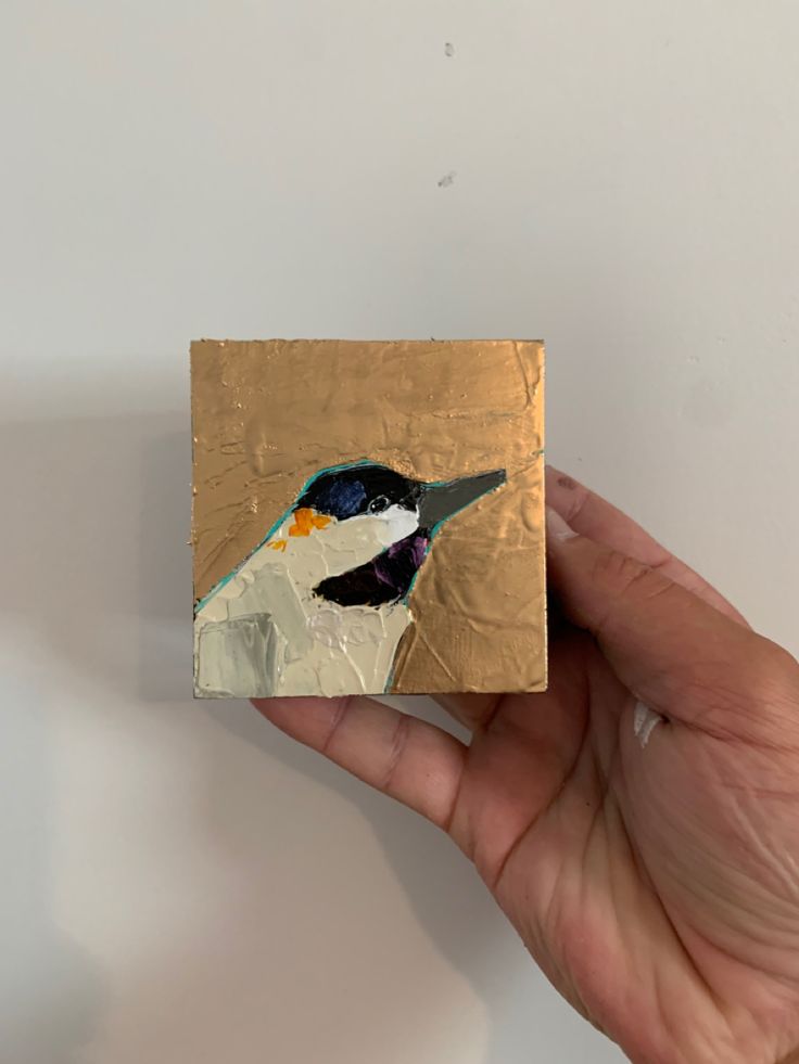 a hand holding a piece of art with a bird painted on it's side