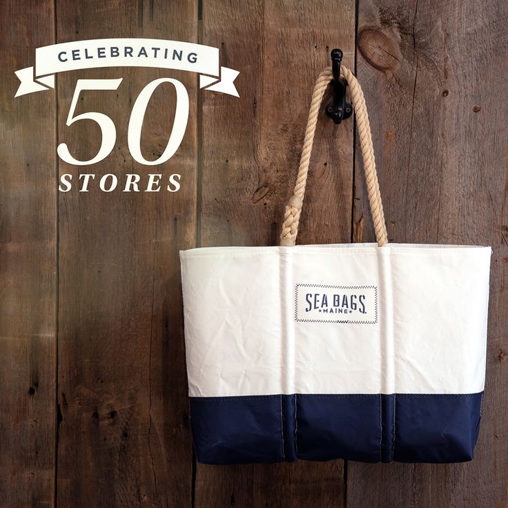 a white and blue tote bag hanging on a wooden wall with the words sea bags celebrating 50 stores