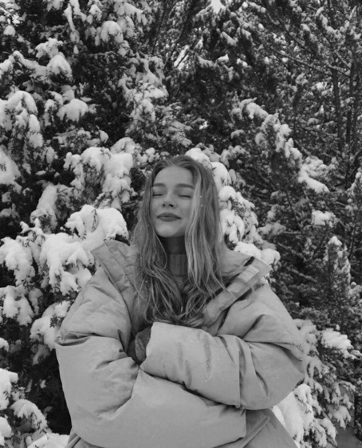 black and white photograph of a woman standing in front of snow - covered trees with her eyes closed