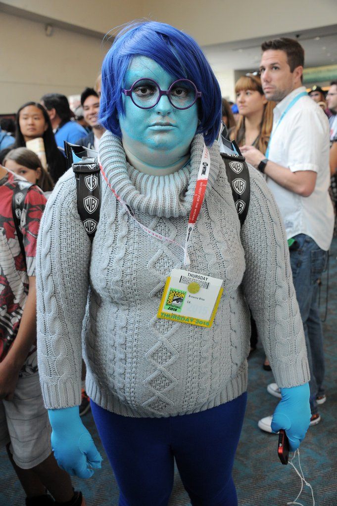 a person with blue hair and glasses in a room full of people