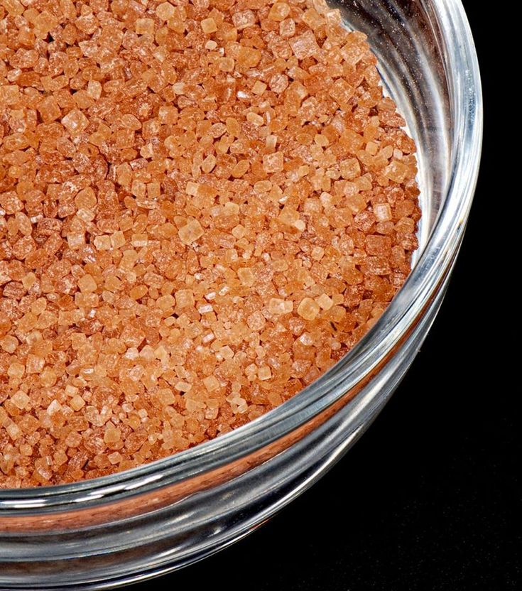 a glass bowl filled with brown sugar on top of a black tablecloth next to a metal spoon