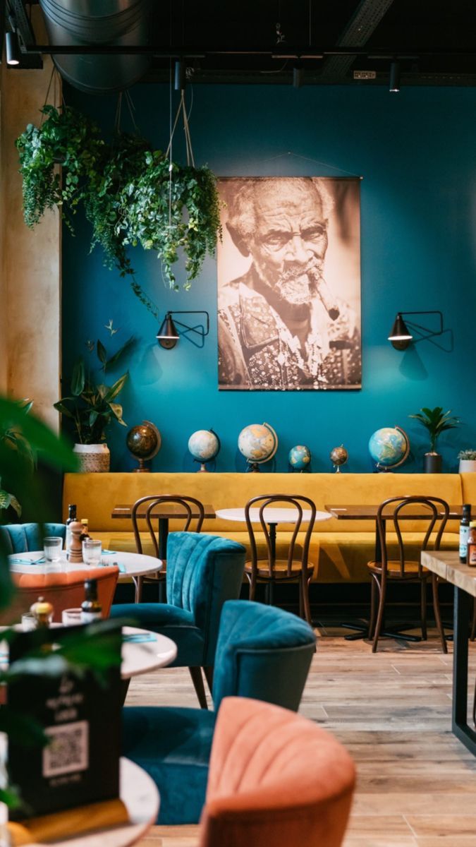 the interior of a restaurant with tables, chairs and plants hanging on the blue wall