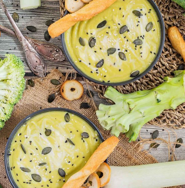 two bowls filled with broccoli and cheese soup on top of a wooden table