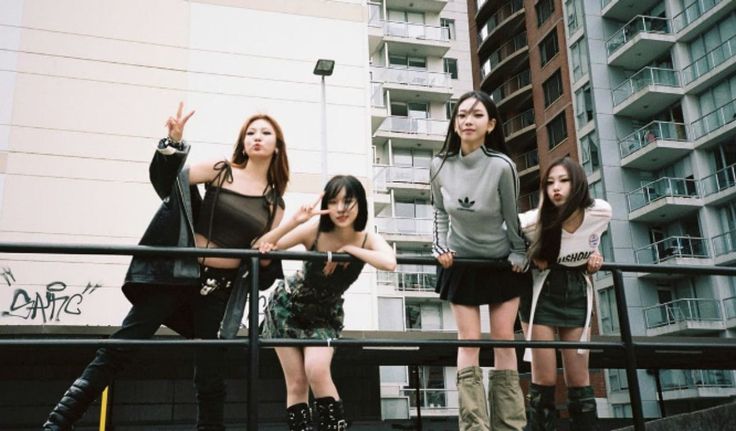 four young women standing on top of stairs in front of tall buildings and one pointing at the sky