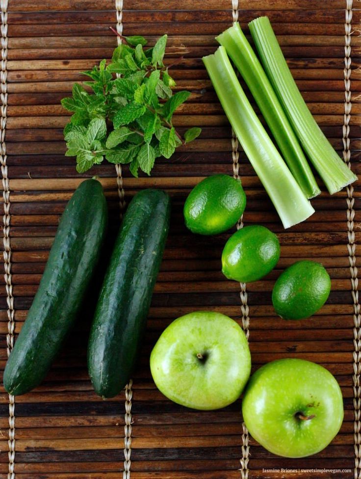 some green vegetables are sitting on a bamboo mat next to cucumbers and celery